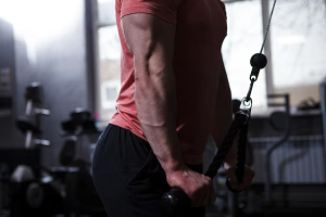 Primer plano de un hombre entrenando en el gimnasio, usando una máquina de poleas para ejercitar los brazos.